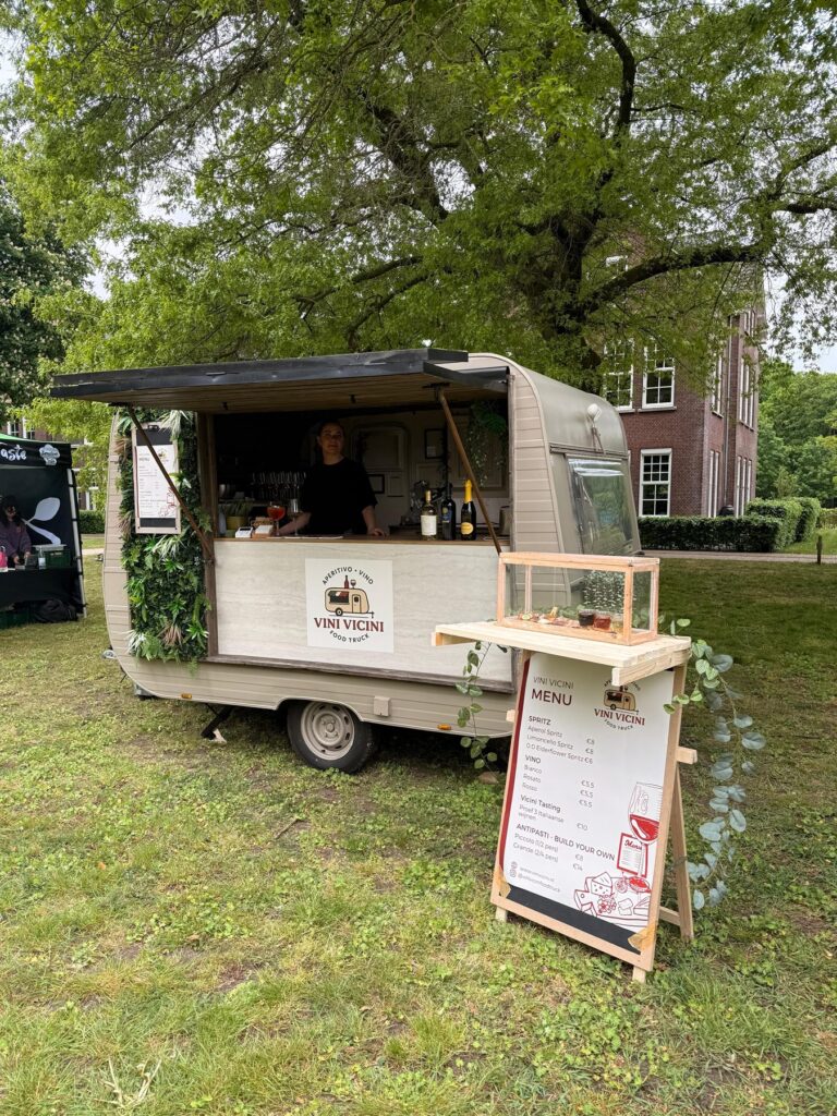 Caravan met menubord onder een grote eik tijdens een tuinfeest